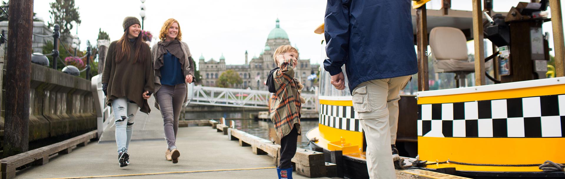 A young child and his mother's chat with a Harbour Ferry Captain on the dock along the Inner Harbour of Victoria, BC