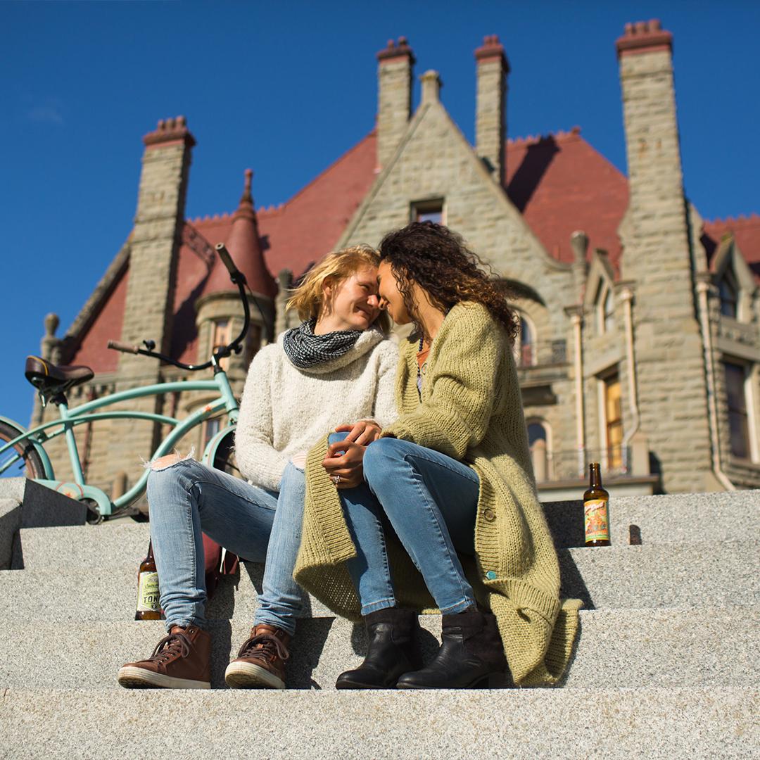 A female couples embraces on the steps outside of Craigdarroch Castle Historic House Museum in Victoria, BC