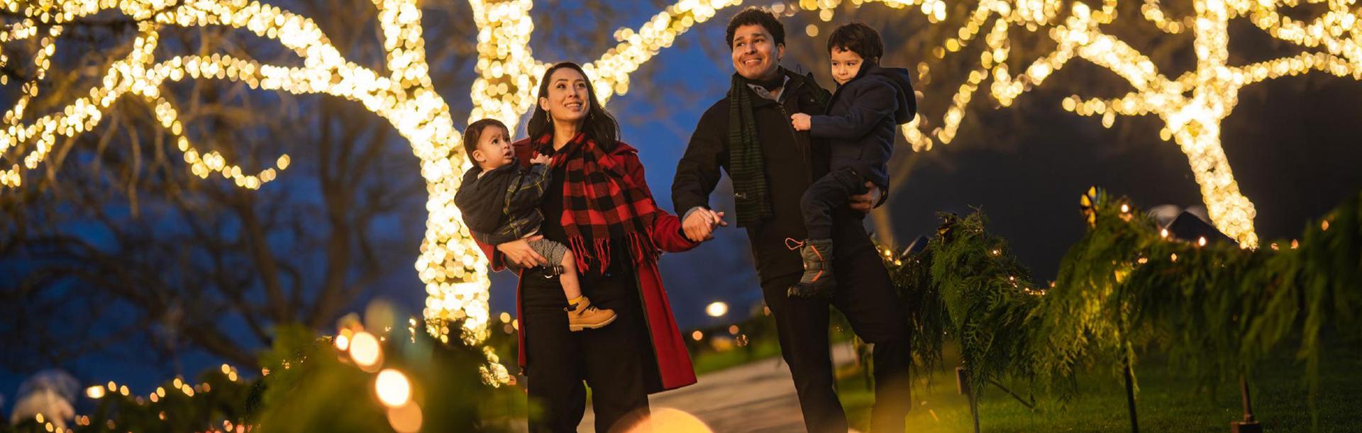 A young family walks hand-in-hand through the holiday light display at The Butchart Gardens in Victoria, BC