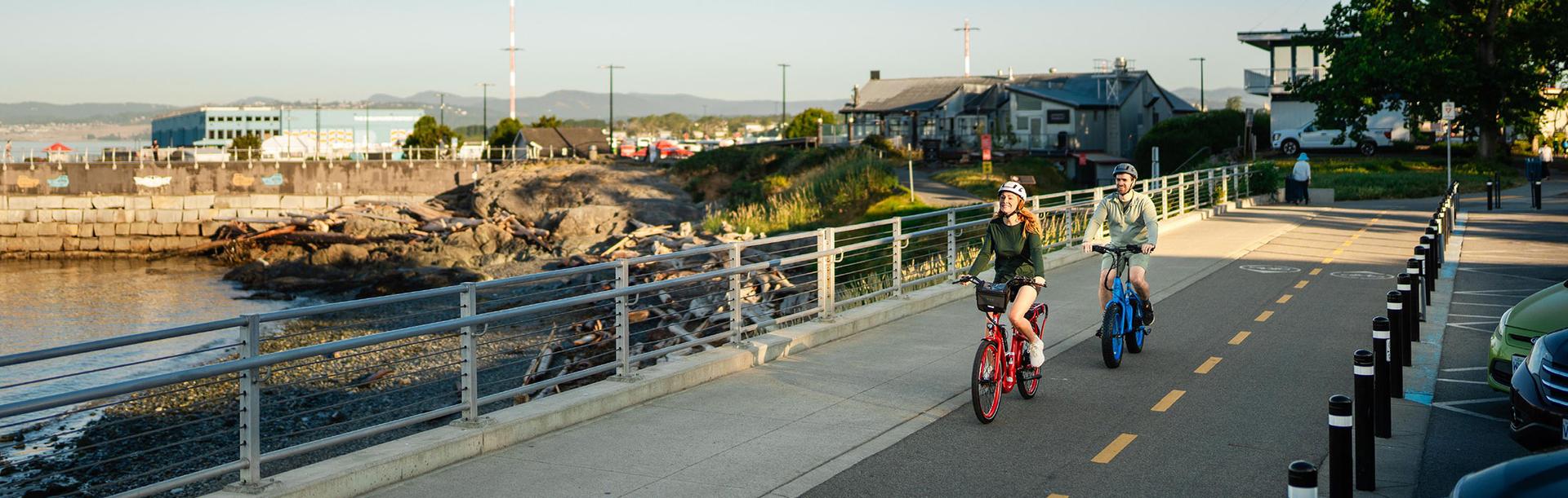 A couple rides e-bikes along a bike lane on Dallas Road in Victoria, BC