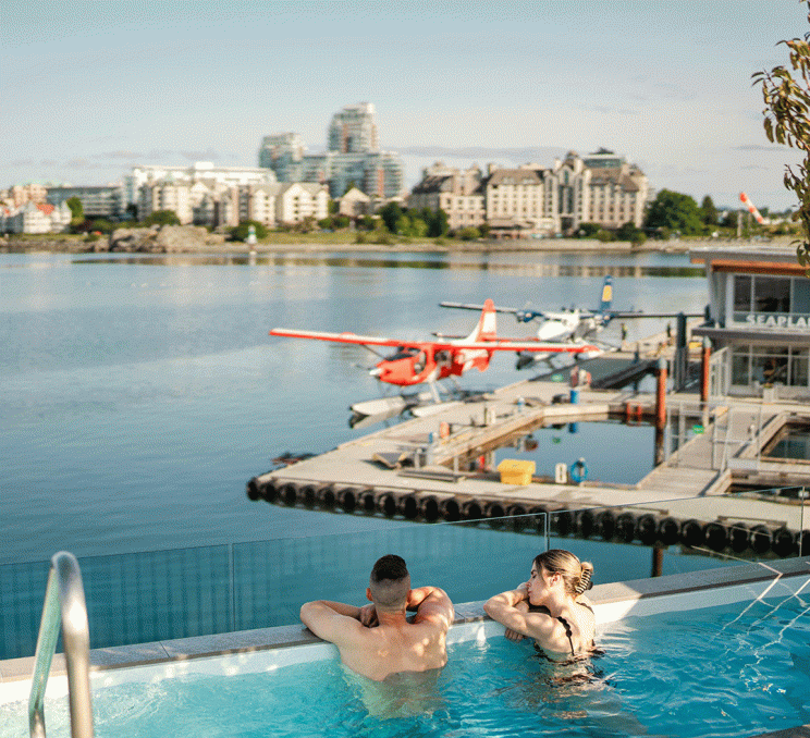 A couple soak in a hot tub overlooking the Inner Harbour and a pair of seaplanes at Havn Saunas in Victoria, BC