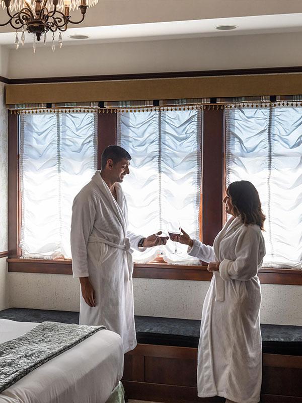 A couple in robes enjoy a glass of wine in their hotel room at Abigail's Hotel in Victoria, BC