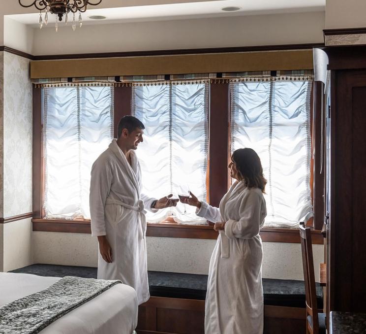 A couple wearing robes enjoy a glass of wine inside a room at Abigail's Hotel in Victoria, BC