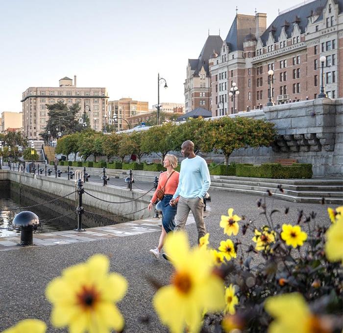 A couple walks hand-in-hand along the Lower Causeway of the Inner Harbour with the Fairmont Empress in the background in Victoria, BC