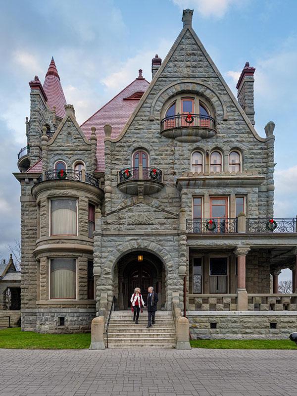 A couple walks hand-in-hand down the staircase out front of Craigdarroch Castle Historic House & Museum during the holidays in Victoria, BC