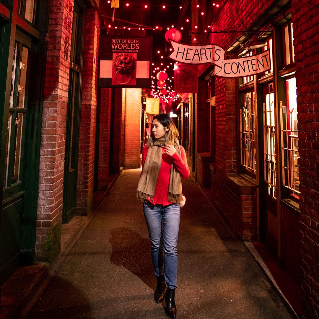 A woman in red walks through Fan Tan Alley at night in Victoria, BC's Chinatown