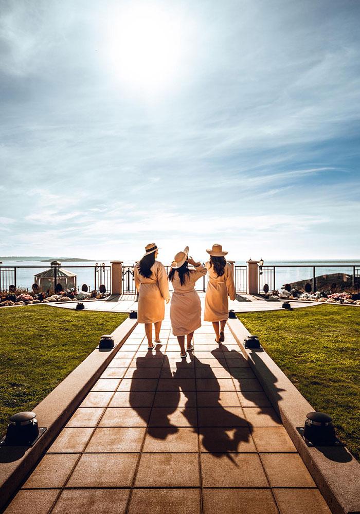 Three women in spa robes walk toward the mineral pools of the Boathouse Spa at the Oak Bay Beach Hotel in Victoria, BC