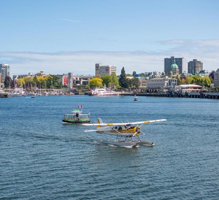 A Kenmore Air seaplane flight taxis across the Inner Harbour of Victoria, BC while a Victoria Harbour Ferry passes in behind it.