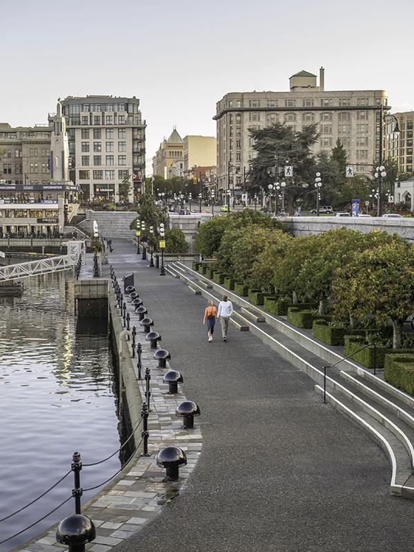 A couple walks hand-in-hand along the Lower Causeway of Victoria, BC's Inner Harbour at sunrise