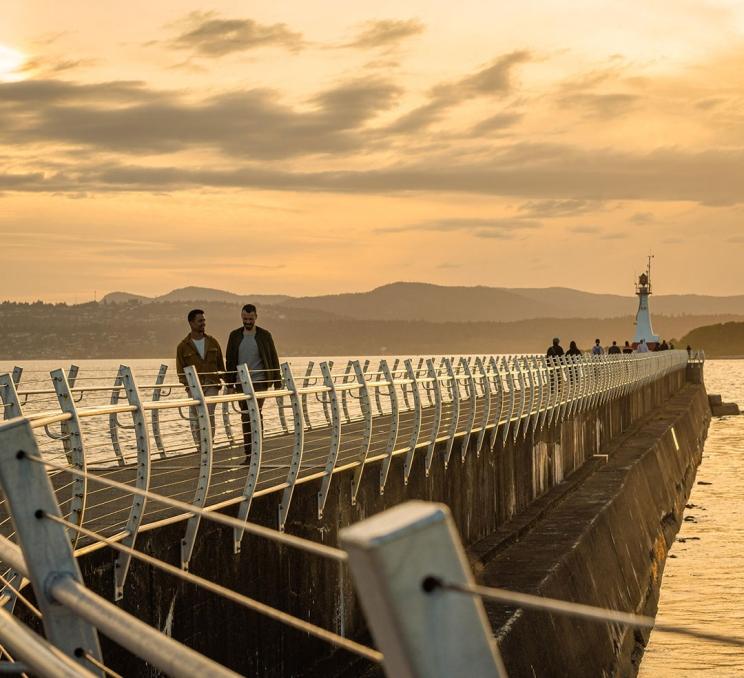 A couple takes a sunset stroll down the Ogden Point Breakwater along the coast of Victoria, BC