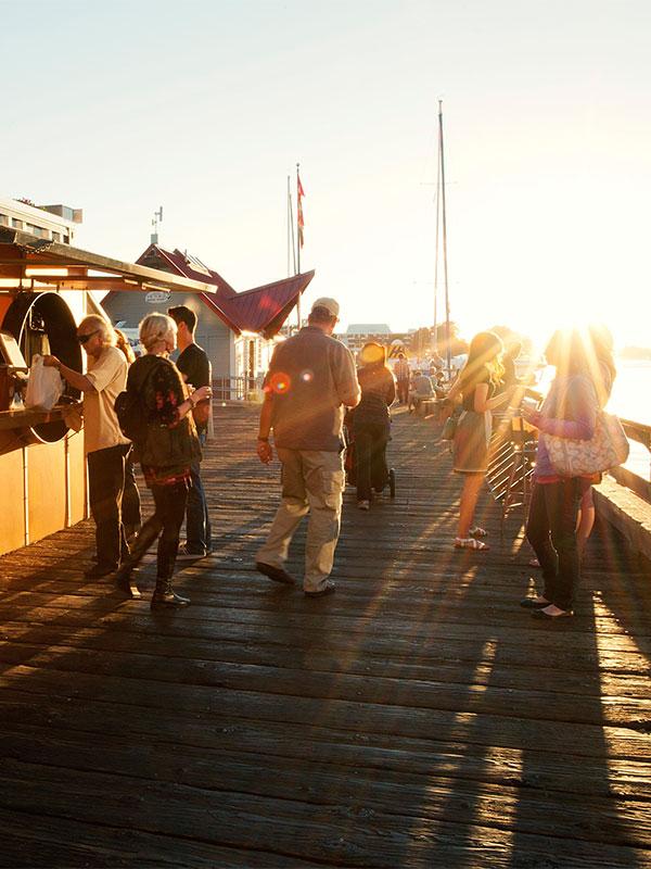 A group of people stroll the dock past Red Fish Blue Fish at sunset in Victoria, BC