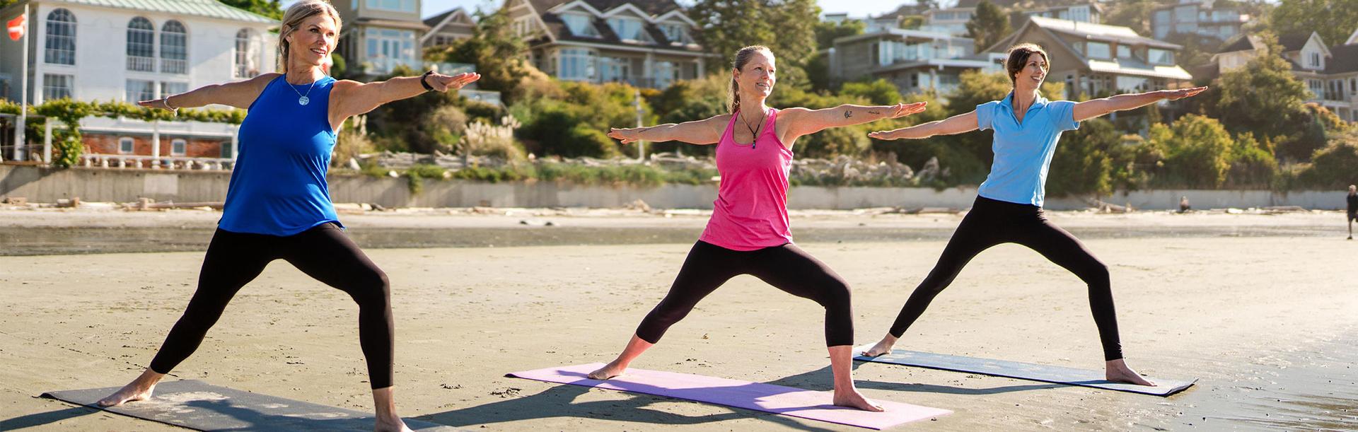 Three women practice yoga on Gonzales Beach during summer in Victoria, BC