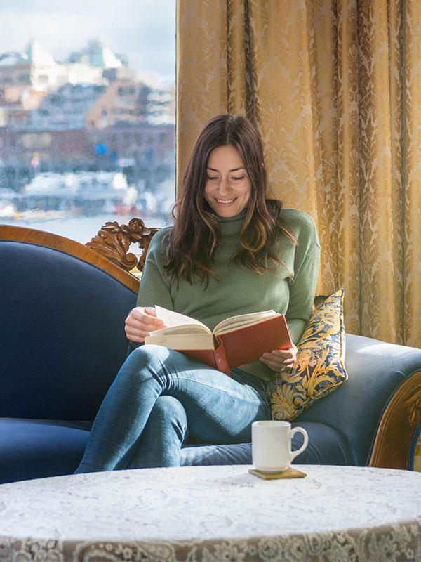 A woman reading a book while enjoying a cup of coffee in her hotel room in Victoria, BC