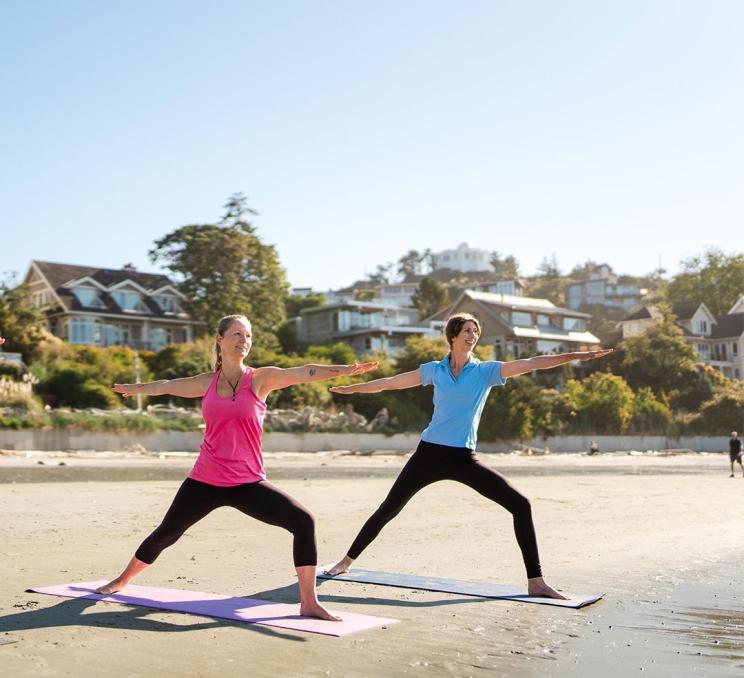 Two women practice yoga on the beach at Gonzales Beach in Victoria, BC