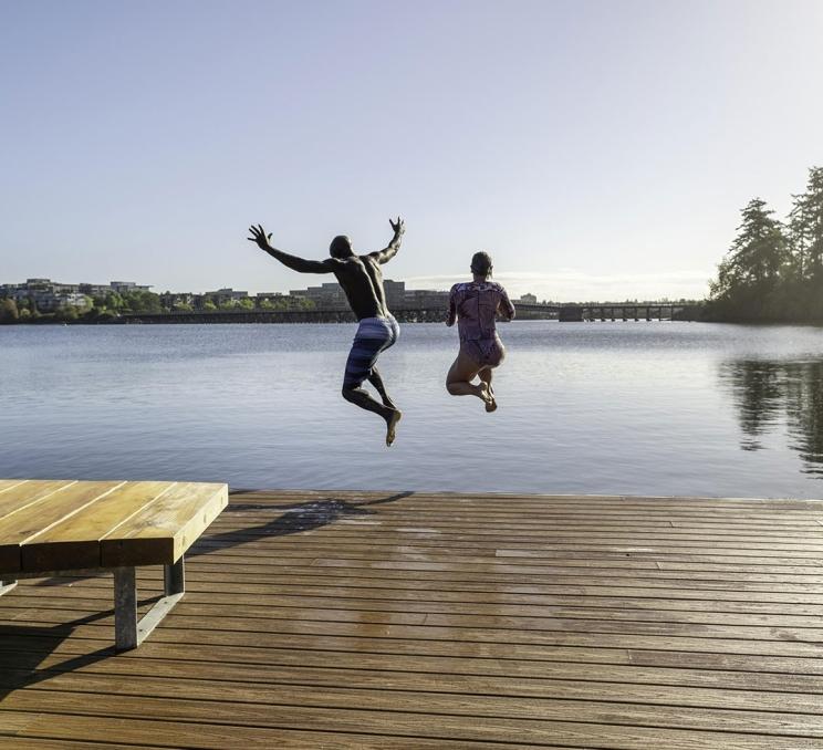 A couple jumps off the end of the dock at Banfield Park in Victoria, BC
