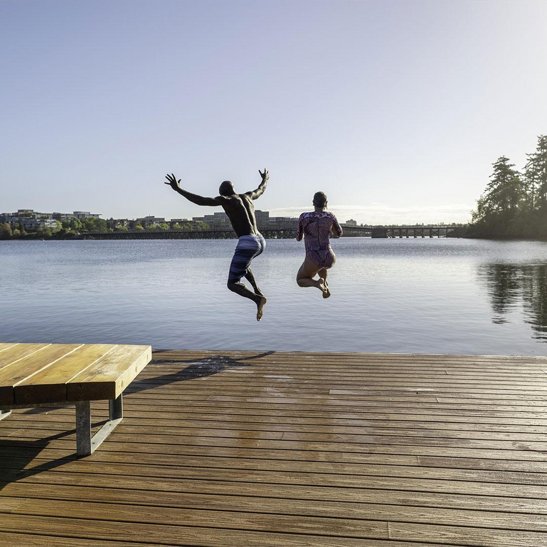 A couple jumps off the end of the dock at Banfield Park in Victoria, BC