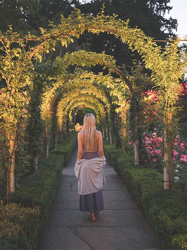 A woman walks below archways along a path at The Butchart Gardens in Victoria, BC