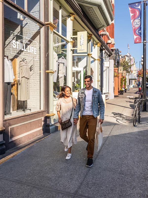 A couple walks hand-in-hand along Lower Johnson Street in Victoria, BC while shopping