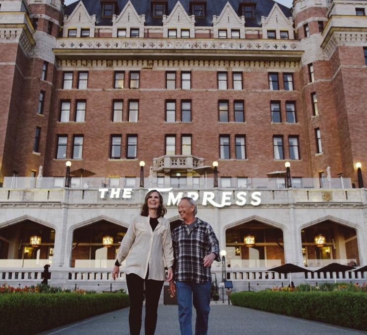 A couple walking down a pathway in front of the Fairmont Empress in Victoria, BC