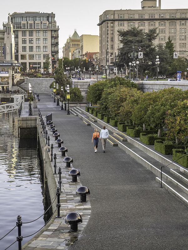 A couple walks along the Lower Causeway of Victoria, BC's Inner Harbour at sunrise