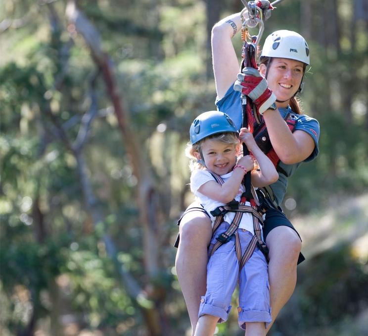 A mother and daughter ride a zipline through the trees