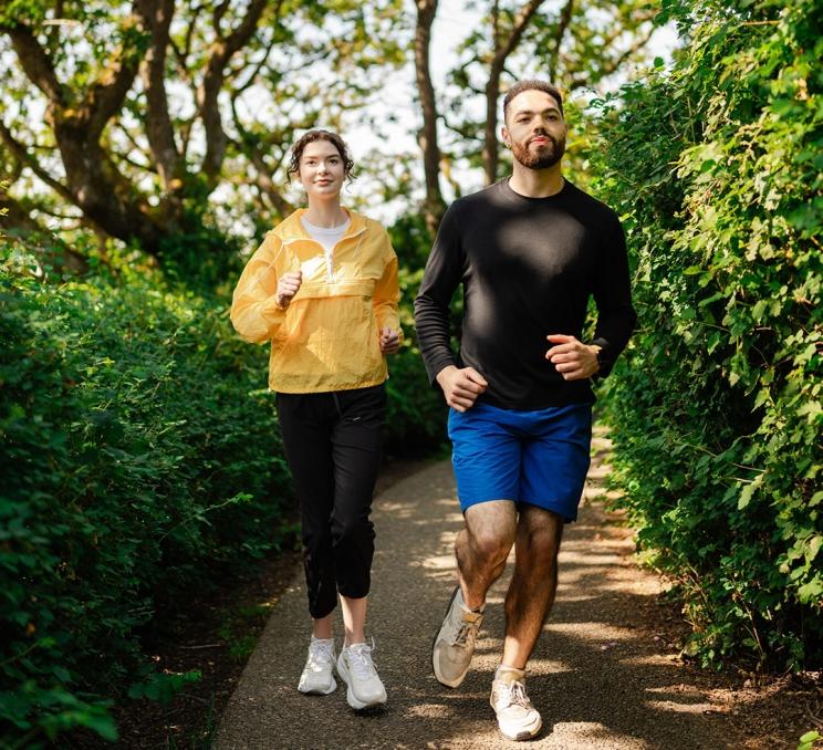 A pair of runners run along the Songhees Walkway through some trees in Victoria, BC's Vic West neighbourhood
