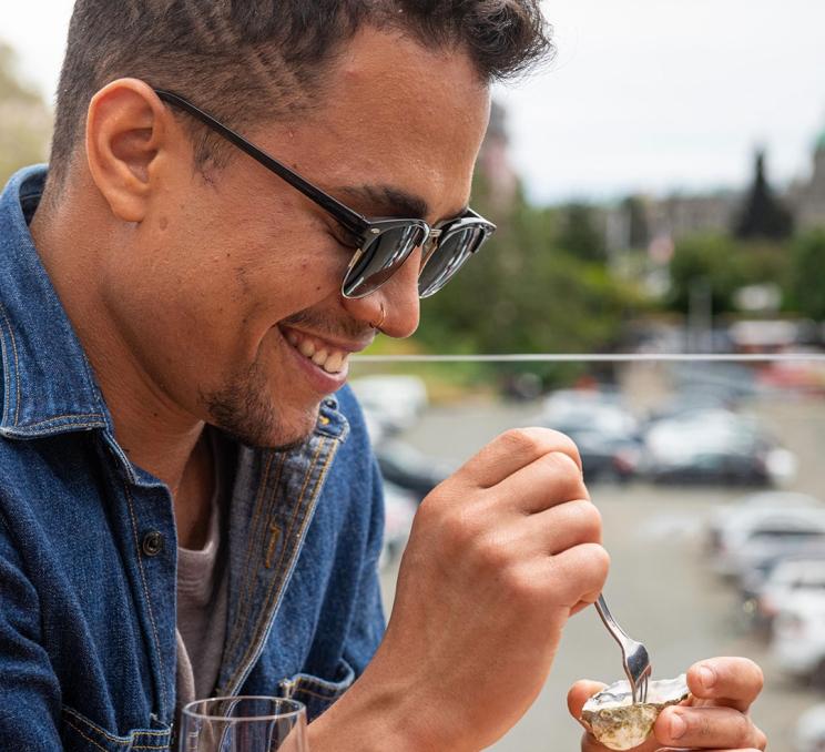 A visitor to Victoria, BC digs into an oyster on the half shell while sitting on the patio at Finn's Seafood, Chops & Cocktails on the Inner Harbour