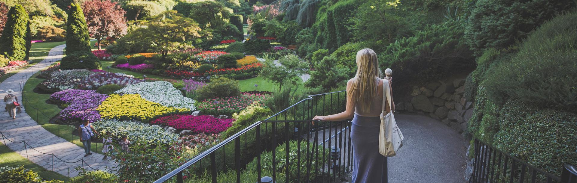 A woman in a dress walks down the stairs into the Sunken Garden of The Butchart Gardens while holding a gelato cone in Victoria, BC