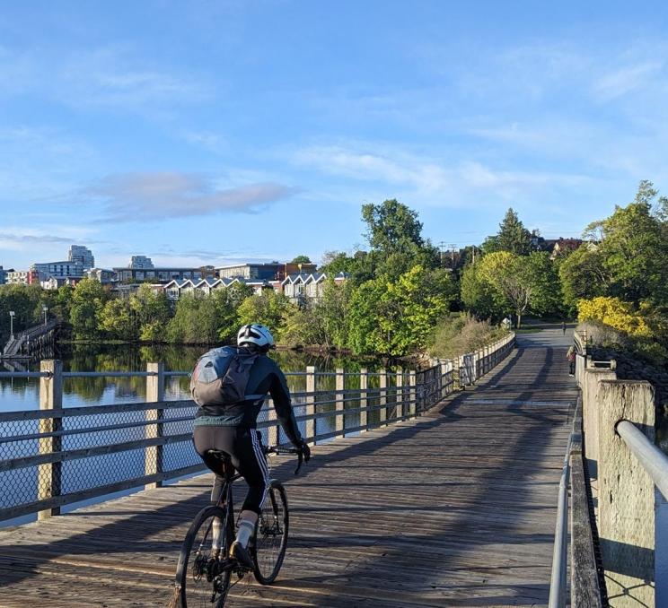 Cyclist riding across Selkirk Trestle on the Galloping Goose Trail in Victoria, BC, overlooking calm water and leafy neighbourhoods