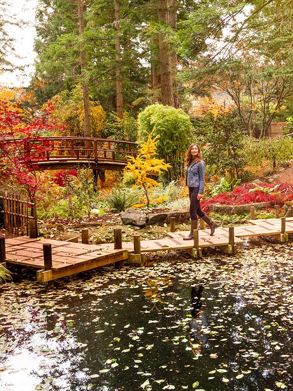 A woman walks along a boardwalk over a pond at the Gardens at HCP in Victoria, BC