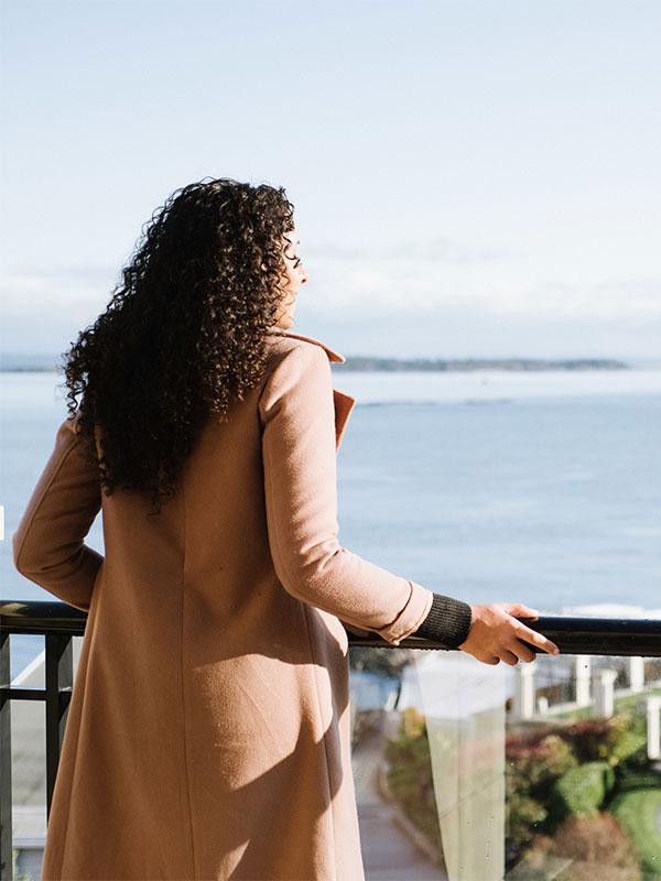 A woman at the Oak Bay Beach Hotel looks over the edge of a balcony out toward the Salish Sea in Victoria, BC