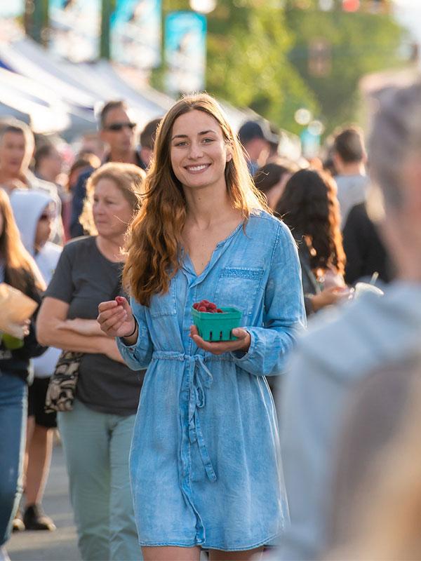 A woman walks through a market with a basket of strawberries in Victoria, BC