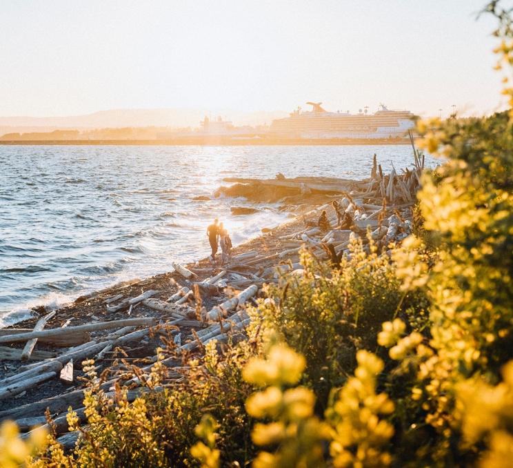 A couple walks along Dallas Road Beach toward Ogden Point at sunset in Victoria, BC