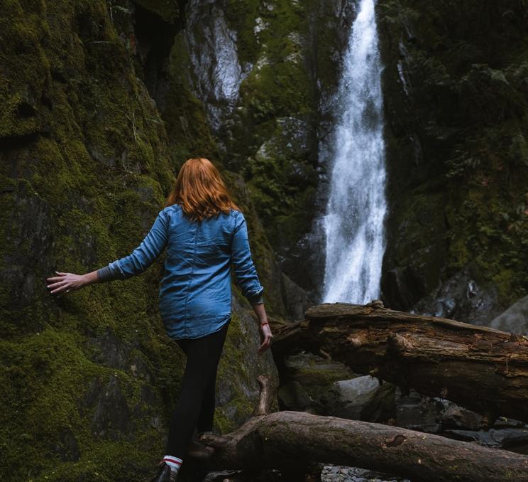 A woman touches the moss on a rock wall while walking toward a waterfall in Goldstream Provincial Park in Victoria, BC