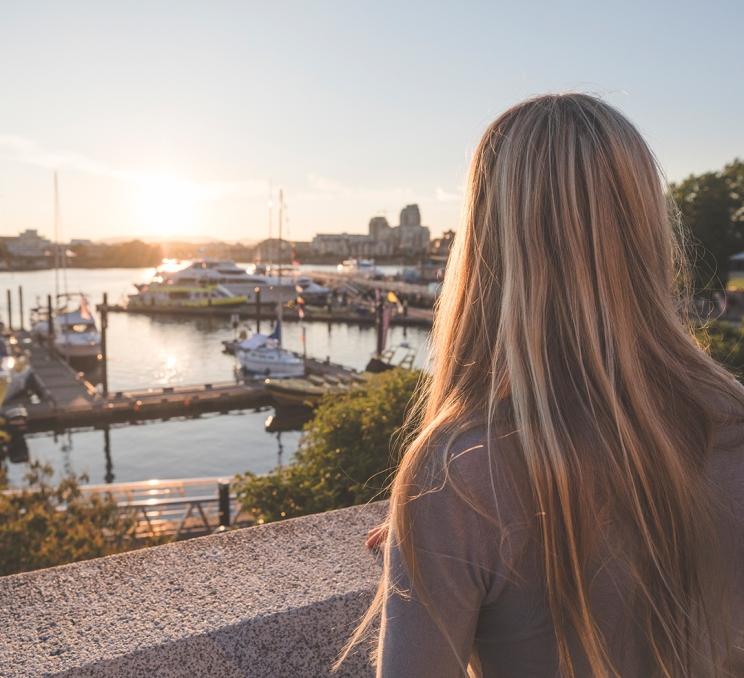 A woman looks out over the Inner Harbour at sunset in Victoria, BC