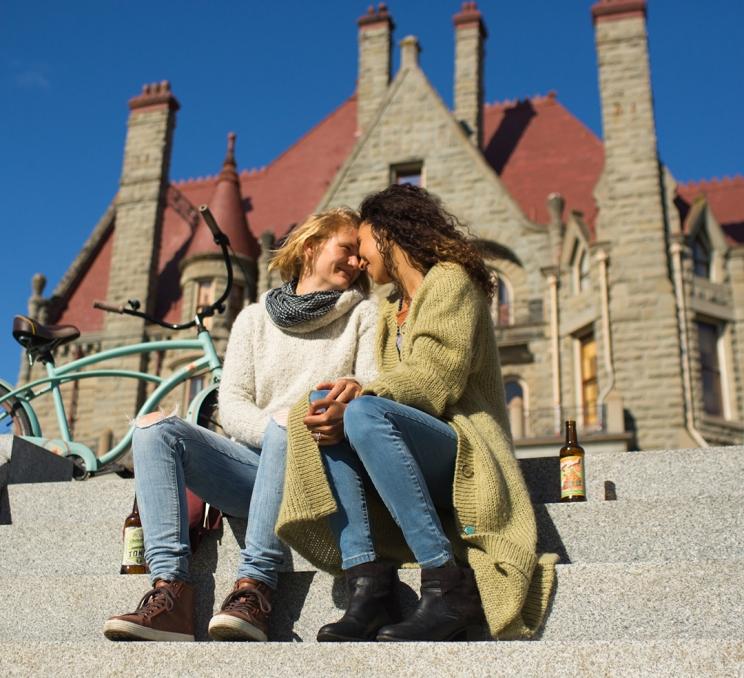 A female couple embraces on the steps outside of Craigdarroch Castle Historic House Museum in Victoria, BC