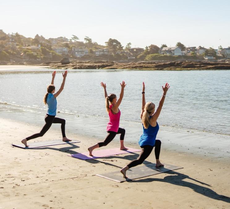 Three women doing yoga on the beach on a sunny day at Gonzales Beach in Victoria, BC