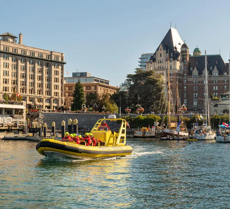 A yellow zodiac boat departs the Inner Harbour for a whale watching tour with the Fairmont Empress in the background in Victoria, BC