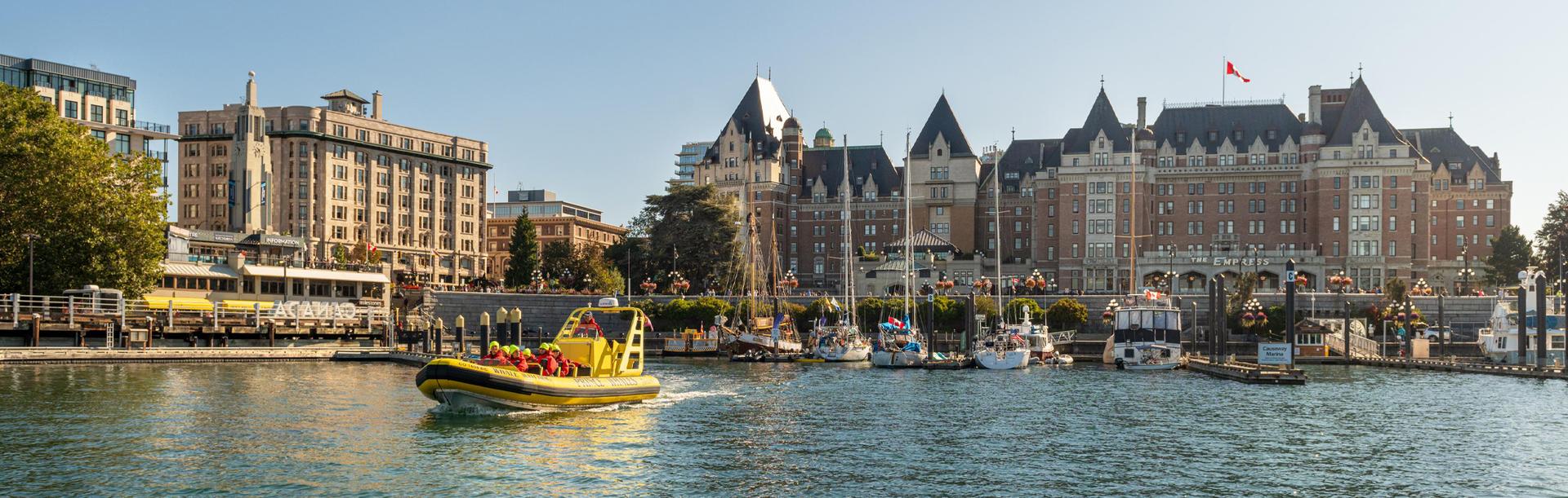 A yellow zodiac boat departs the Inner Harbour for a whale watching tour with the Fairmont Empress in the background in Victoria, BC